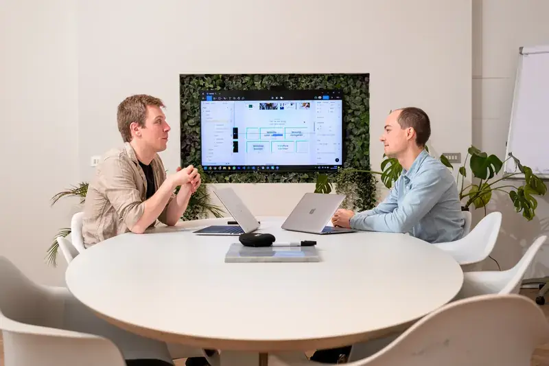 Twee teamleden van upshift bespreken samen een digitaal project aan tafel.